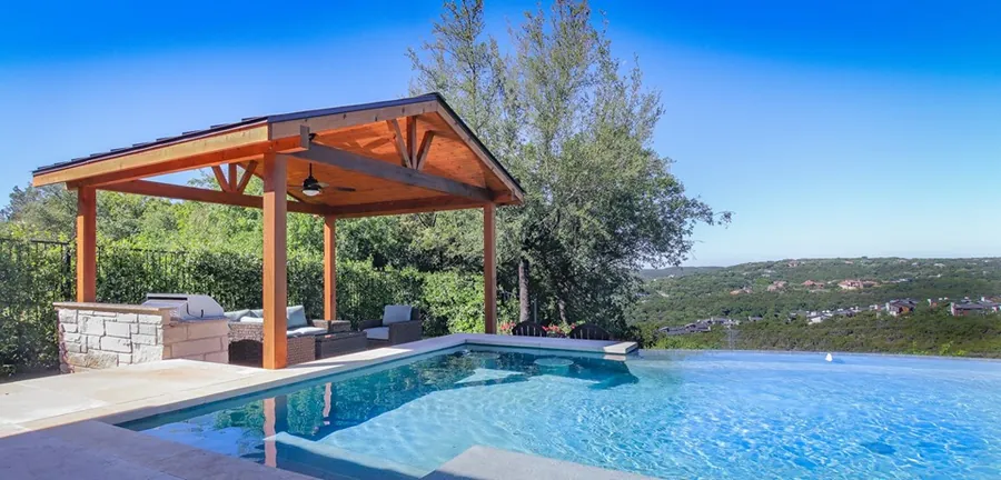 Freestanding cedar pavilion with a full outdoor kitchen and tongue and groove ceiling by an infinity pool