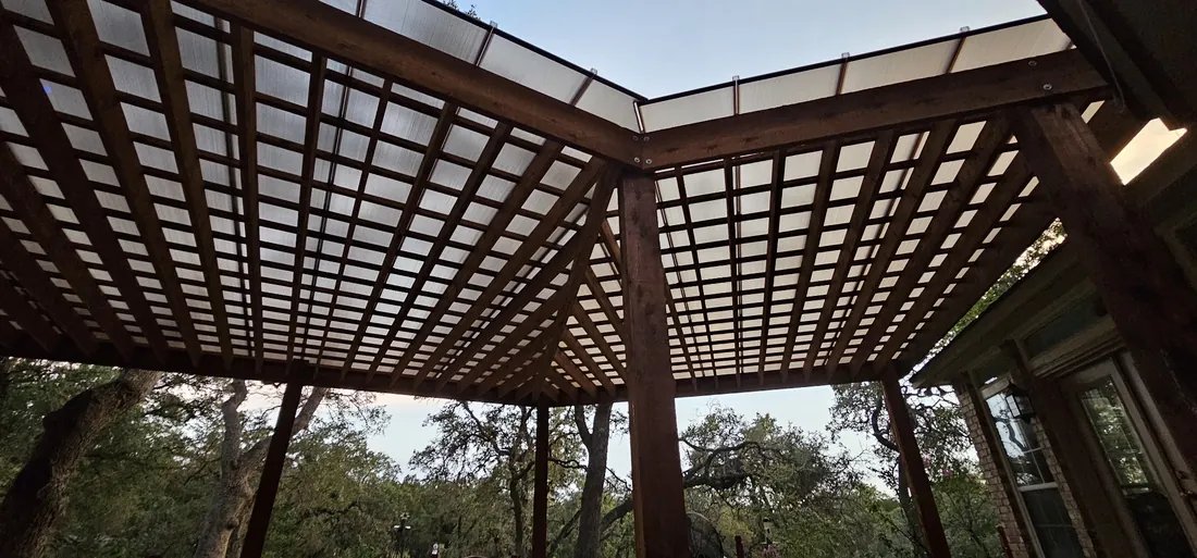 Underside view of a custom-shape cedar pergola with a polycarbonate roof