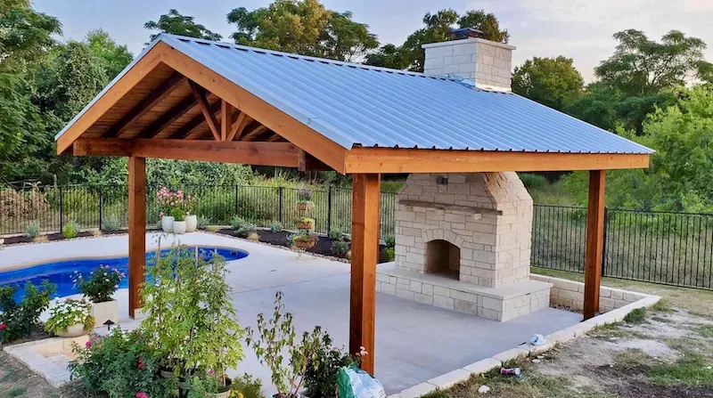 24-foot square cedar pavilion with a Galvalume R-panel metal roof and a stone fireplace built through the roof
