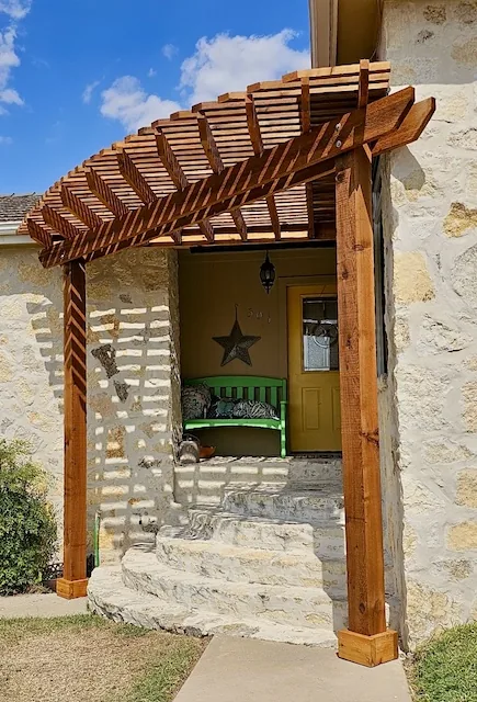 Custom-shape stained cedar pergola over a stone home entryway